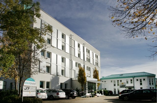 A modern, multi-story hotel building surrounded by trees. Cars are parked in front of the entrance. A sign with the hotel's name is visible., © ateckhotel A modern, multi-story hotel building surrounded by trees. Cars are parked in front of the entrance. A sign with the hotel's name is visible., © ateckhotel