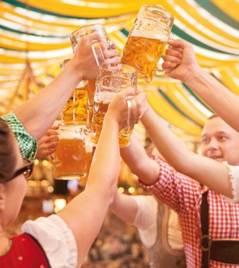 Group in traditional costume toasting with beer mugs in a festively decorated beer tent. A cheerful atmosphere under yellow and green fabric panels., © SMG, Jean-Claude Winkler