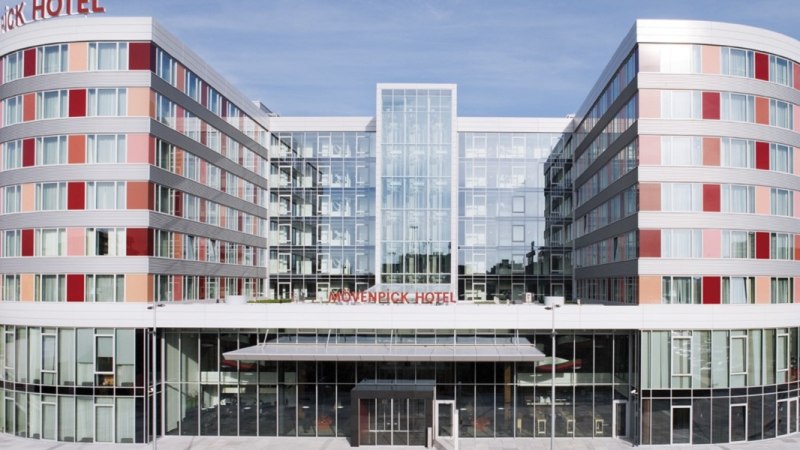 The Mövenpick Hotel Stuttgart Airport has a modern glass façade with rounded corners and red accents., © Mövenpick Hotel Stuttgart Airport The Mövenpick Hotel Stuttgart Airport has a modern glass façade with rounded corners and red accents., © Mövenpick Hotel Stuttgart Airport