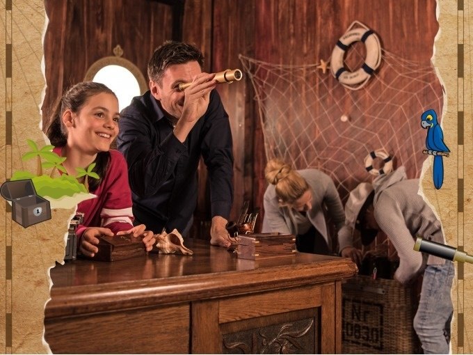 People in a pirate-themed room. A man looks through a telescope while others search for clues. Decorations such as a lifebuoy and net are visible., &copy; ExitGames Stuttgart