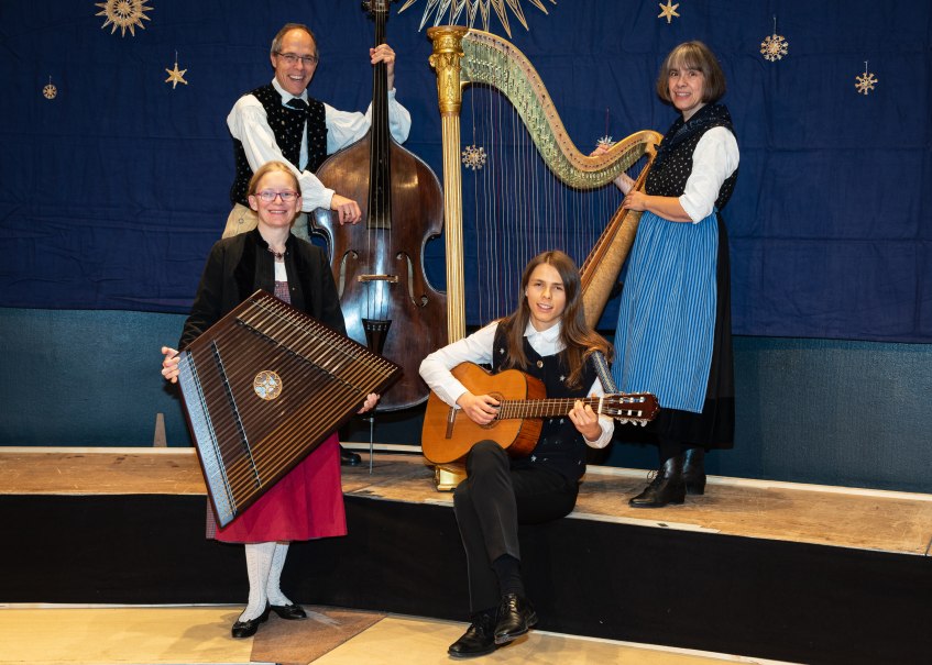 Vier Musiker in traditioneller Kleidung spielen Kontrabass, Zither, Gitarre und Harfe vor einem blauen Hintergrund mit Sternendekoration., &copy; Peter Oehl