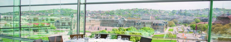 Ein runder Tisch mit weißer Tischdecke und Gläsern steht in einem verglasten Raum mit Blick auf eine Stadt und historische Gebäude., © Stuttgart-Marketing GmbH