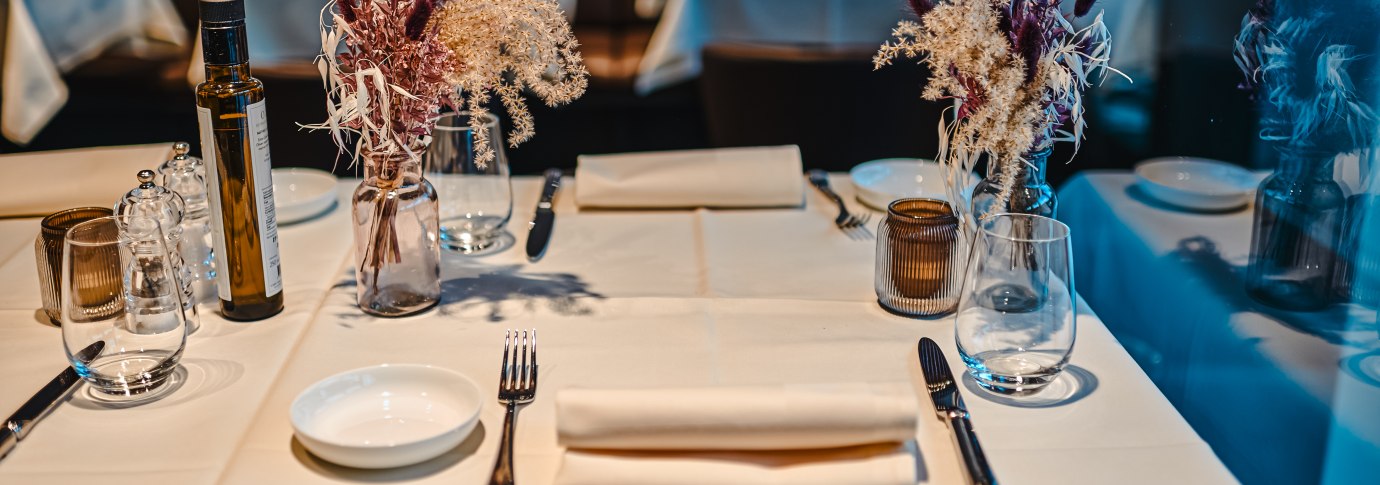 Ein elegant gedeckter Tisch in einem Restaurant mit wei&szlig;en Tischdecken, Blumenarrangement, Gl&auml;sern und Besteck., &copy; Feinkost B&ouml;hm GmbH