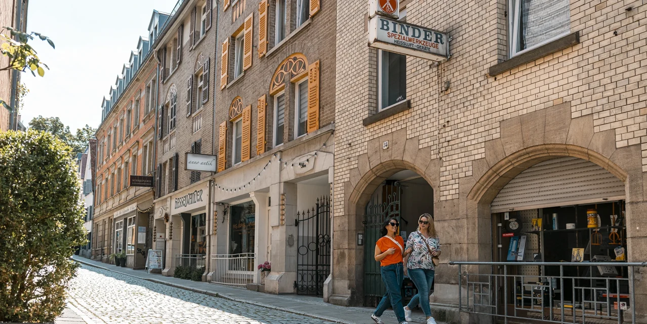Zwei Frauen spazieren durch das Bohnenviertel in einer sonnigen Altstadtgasse mit historischen Fassaden und Ladenfronten., © SMG, Sarah Schmid Zwei Frauen spazieren durch das Bohnenviertel in einer sonnigen Altstadtgasse mit historischen Fassaden und Ladenfronten., © SMG, Sarah Schmid