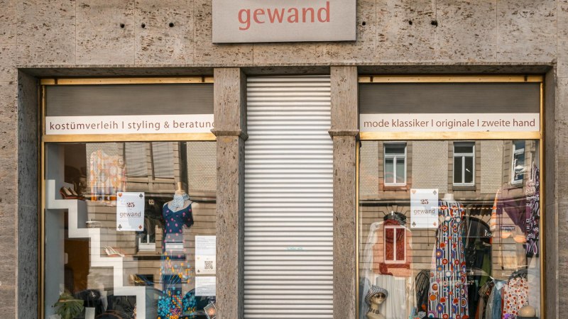 Schaufenster des Ladens 'gewand' mit bunten Kleidern und Accessoires. Schilder weisen auf Kostümverleih, Styling und Second-Hand-Mode hin., © SMG, Sarah Schmid