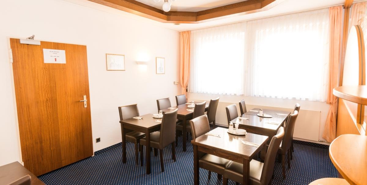 Heller Frühstücksraum mit mehreren Tischen und Stühlen, blauer Teppichboden und große Fenster mit Vorhängen., © ARNOTEL GmbH