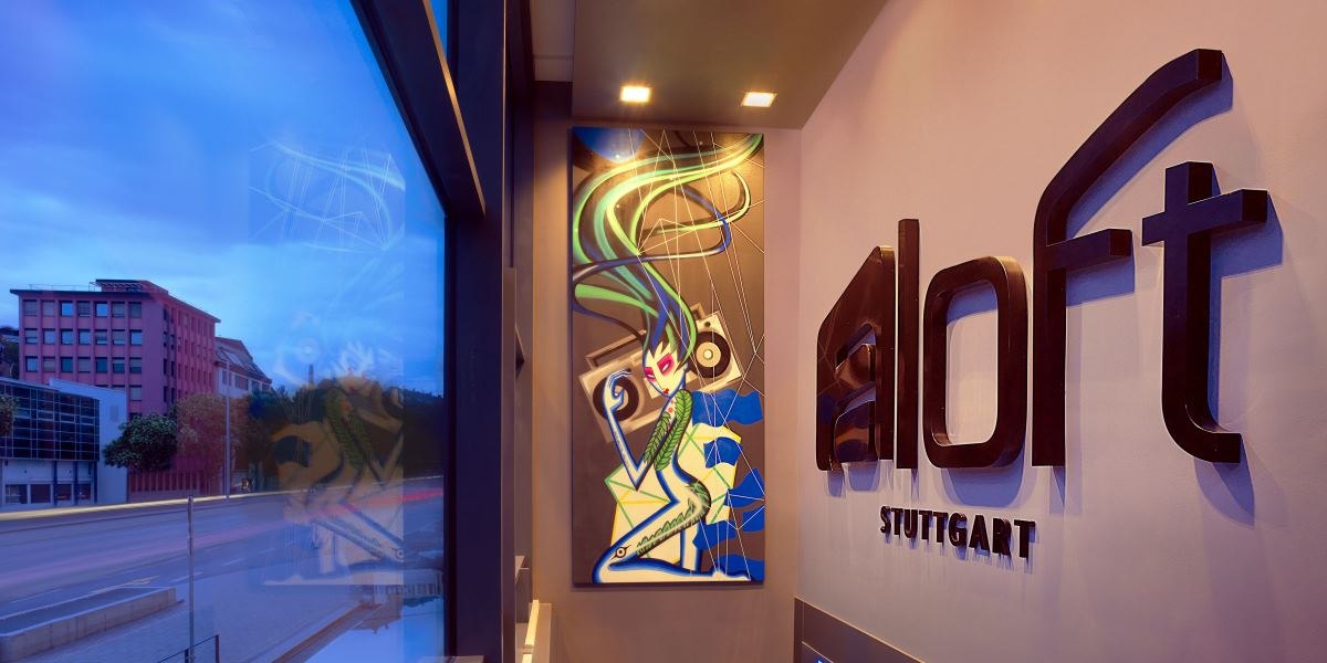 Eingangsbereich des Aloft Stuttgart Hotels mit einem modernen Kunstwerk an der Wand und dem Hotelnamen "aloft Stuttgart" in großen Buchstaben., © Aloft Stuttgart