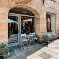 Ein kleines Ladengeschäft mit Schaufenster, dekoriert mit Kleidung. Davor stehen zwei weiße Stühle und ein Tisch auf dem Gehweg., © MAGASIN Geißstrasse 15, Stuttgart Ein kleines Ladengeschäft mit Schaufenster, dekoriert mit Kleidung. Davor stehen zwei weiße Stühle und ein Tisch auf dem Gehweg., © MAGASIN Geißstrasse 15, Stuttgart
