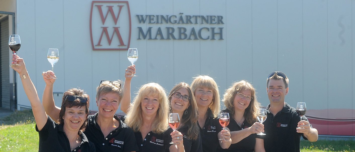 Sieben Personen heben lächelnd Weingläser vor einem Gebäude mit 'Weingärtner Marbach'-Logo., © Weingärtner Marbach e. G.