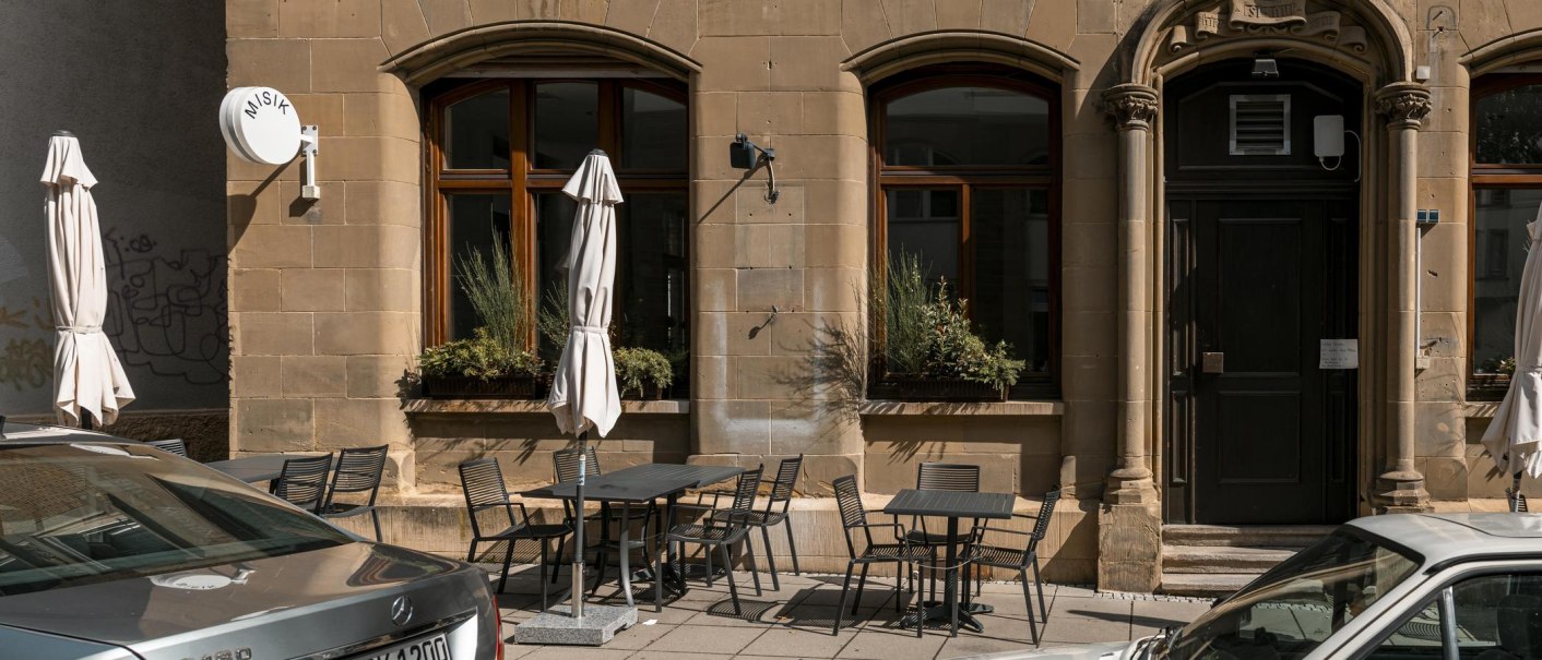 Building with tables and chairs on the sidewalk, sunshades and a sign with 'MISIK'. Historic façade with large windows., © SMG Stuttgart Marketing GmbH - Sarah Schmid