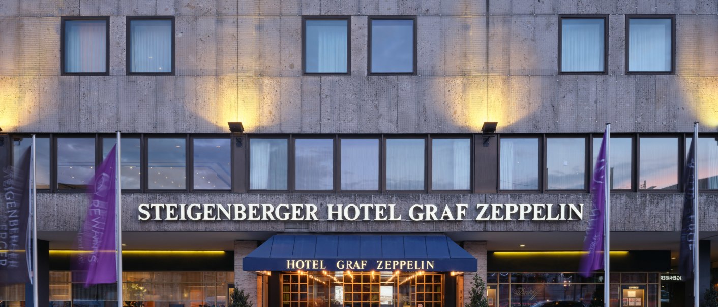 Exterior view of the Steigenberger Hotel Graf Zeppelin with illuminated entrance and flags., © Steigenberger Graf Zeppelin