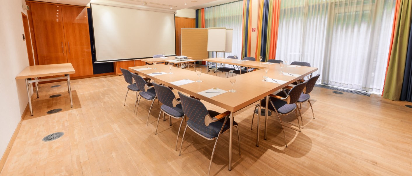 Meeting room with U-shaped table, chairs, flipchart and projector. Light-colored curtains and a wooden floor create a professional atmosphere., © PLAZA Hotelgroup GmbH