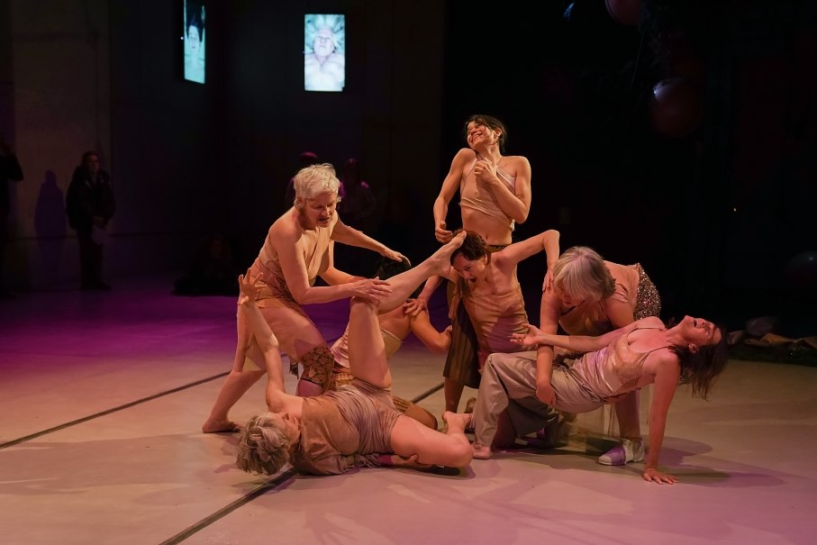 Eine Tanzgruppe in hautfarbenen Kostümen führt eine dynamische Performance auf einer Bühne auf. Die Beleuchtung ist gedämpft und dramatisch., © © Daniela Wolf