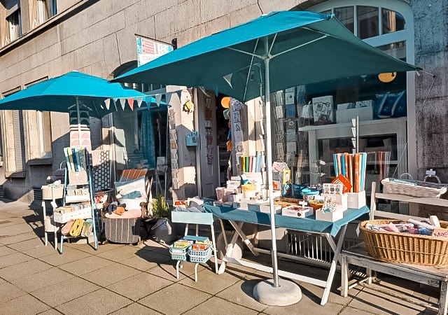 A store in the south of Stuttgart with blue parasols. Fabric items and decorations are displayed on tables and chairs outside., © Cosima Chiton, Stuttgart