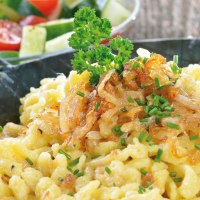Cheese spaetzle with fried onions and chives in a pan, served with a fresh salad of tomatoes and cucumber., © kab-vision - Fotolia Cheese spaetzle with fried onions and chives in a pan, served with a fresh salad of tomatoes and cucumber., © kab-vision - Fotolia