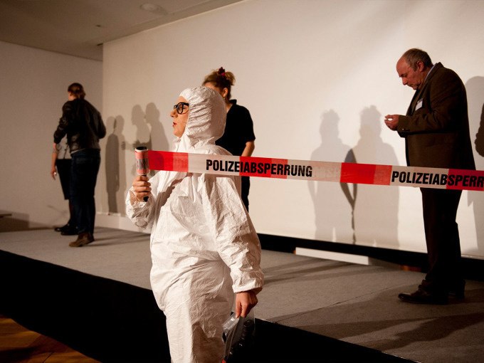 Person in protective suit in front of police cordon, other people in the background on a stage. Scene looks like a detective story in a museum., © Landesmuseum Württemberg Person in protective suit in front of police cordon, other people in the background on a stage. Scene looks like a detective story in a museum., © Landesmuseum Württemberg