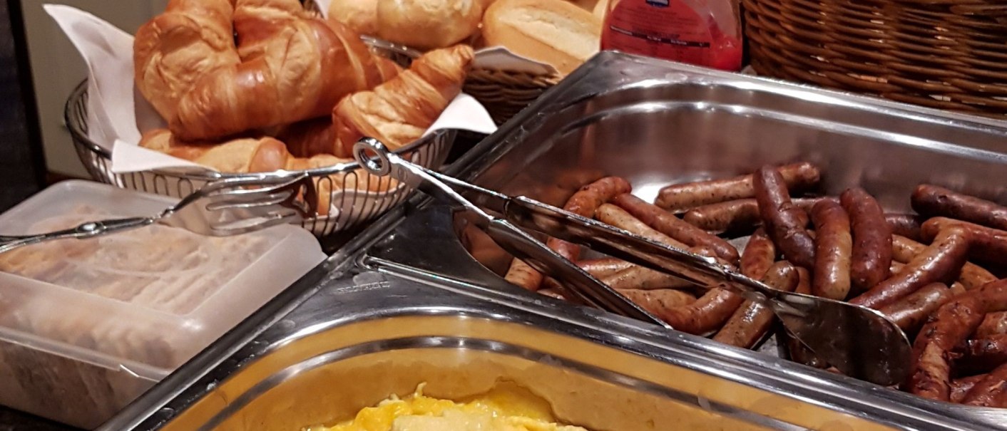 A breakfast buffet featuring scrambled eggs, sausages, rolls, and croissants in a cozy hotel restaurant., &copy; Hotel Spahr