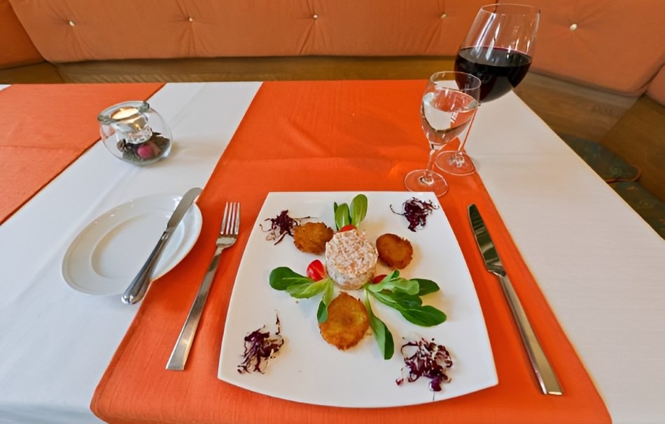 Appetizer on a white plate with salad and vegetables, decorated on an orange and white tablecloth. A glass of red wine and water are placed next to it., © Hotel Neuwirtshaus Appetizer on a white plate with salad and vegetables, decorated on an orange and white tablecloth. A glass of red wine and water are placed next to it., © Hotel Neuwirtshaus