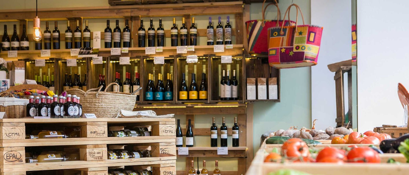 Delicatessen with wine racks, baskets and fresh vegetables. Wooden pallets as shelves, colorful bags on the wall, warm lighting., © Benjamin Stollenberg