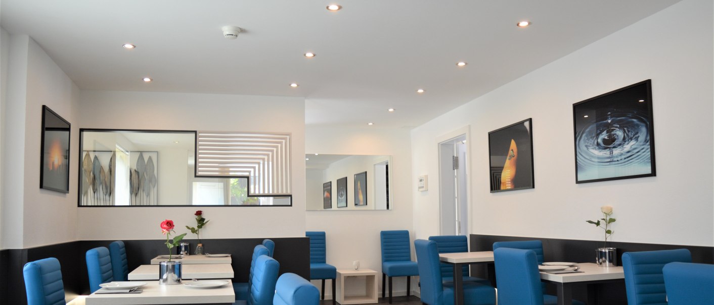 Moderner Frühstücksraum mit blauen Stühlen, weißen Tischen und dekorativen Bildern an den Wänden. Dezente Beleuchtung und stilvolle Dekoration., © Hotel BaWü Moderner Frühstücksraum mit blauen Stühlen, weißen Tischen und dekorativen Bildern an den Wänden. Dezente Beleuchtung und stilvolle Dekoration., © Hotel BaWü