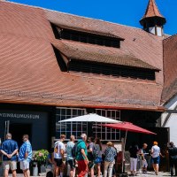 Visitors stand in front of the wine museum in Uhlbach. The half-timbered building has a red tiled roof. Vineyards can be seen in the background., © Stuttgart-Marketing GmbH, Thomas Niedermüller