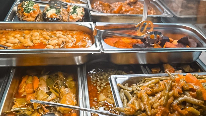 A buffet with various hot dishes in stainless steel containers, including beans, vegetables and stuffed eggplants., © Zauberküche, Stuttgart