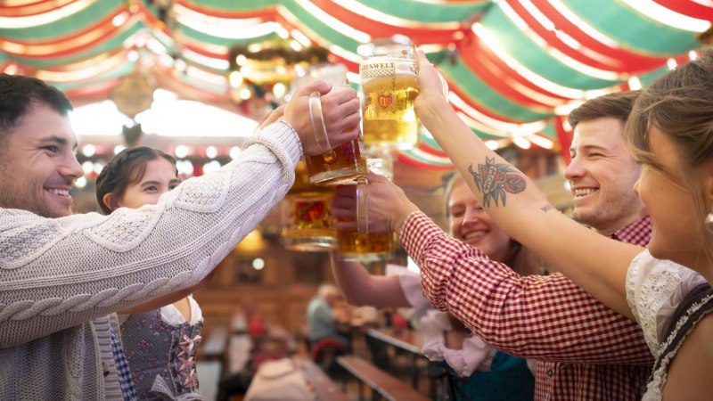 People in traditional dress clink glasses with mugs of beer in a festively decorated tent. Cheerful atmosphere at a folk festival., &copy; Stuttgart-Marketing GmbH, Sarah Schmid