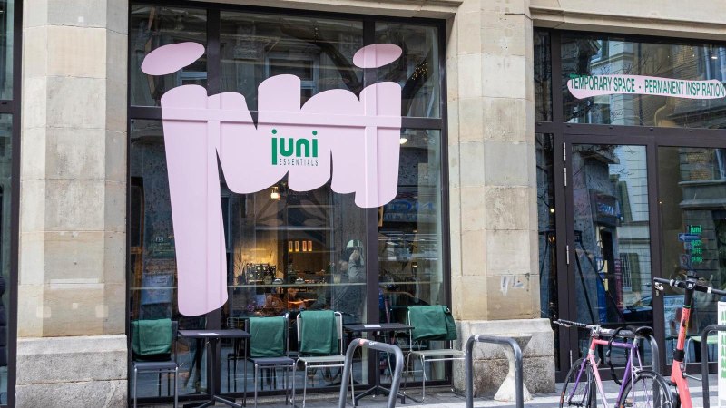 A caf&eacute; with large windows and the words 'juni essentials'. In front of it are bicycles and tables with chairs., &copy; SMG, Sarah Schmid