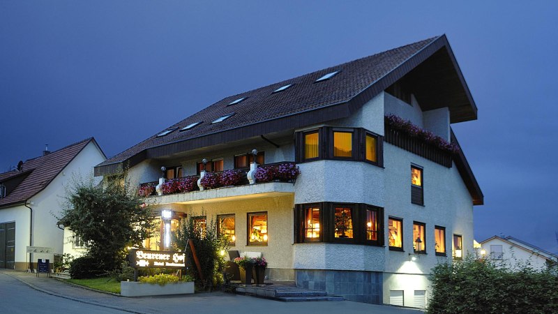 Beleuchtetes Geb&auml;ude bei Nacht mit Blumen auf dem Balkon und einem Schild "Beurener Hof". Der Himmel ist dunkelblau., &copy; Hotel & Restaurant Beurener Hof