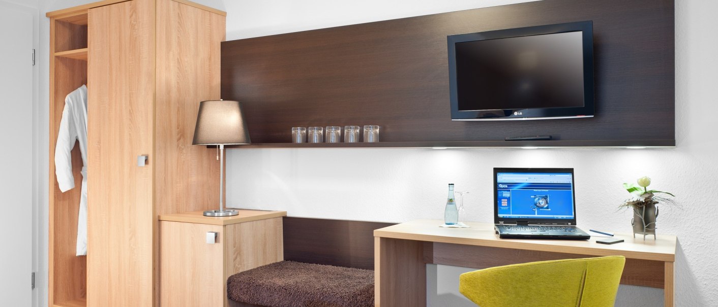 A modern hotel room with a desk, laptop, yellow chair, TV, closet, and lamp., &copy; TOMAS