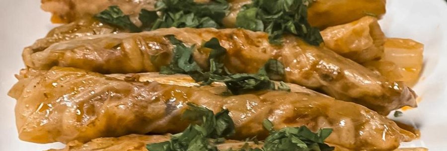 Stuffed cabbage rolls on a plate, garnished with fresh herbs. They are golden brown and appetizingly presented., © Zauberküche, Stuttgart