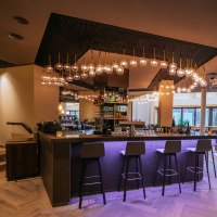 Modern bar with stylish lighting, high stools and cozy seating areas. The atmosphere is inviting and elegant., © Breuninger Modern bar with stylish lighting, high stools and cozy seating areas. The atmosphere is inviting and elegant., © Breuninger
