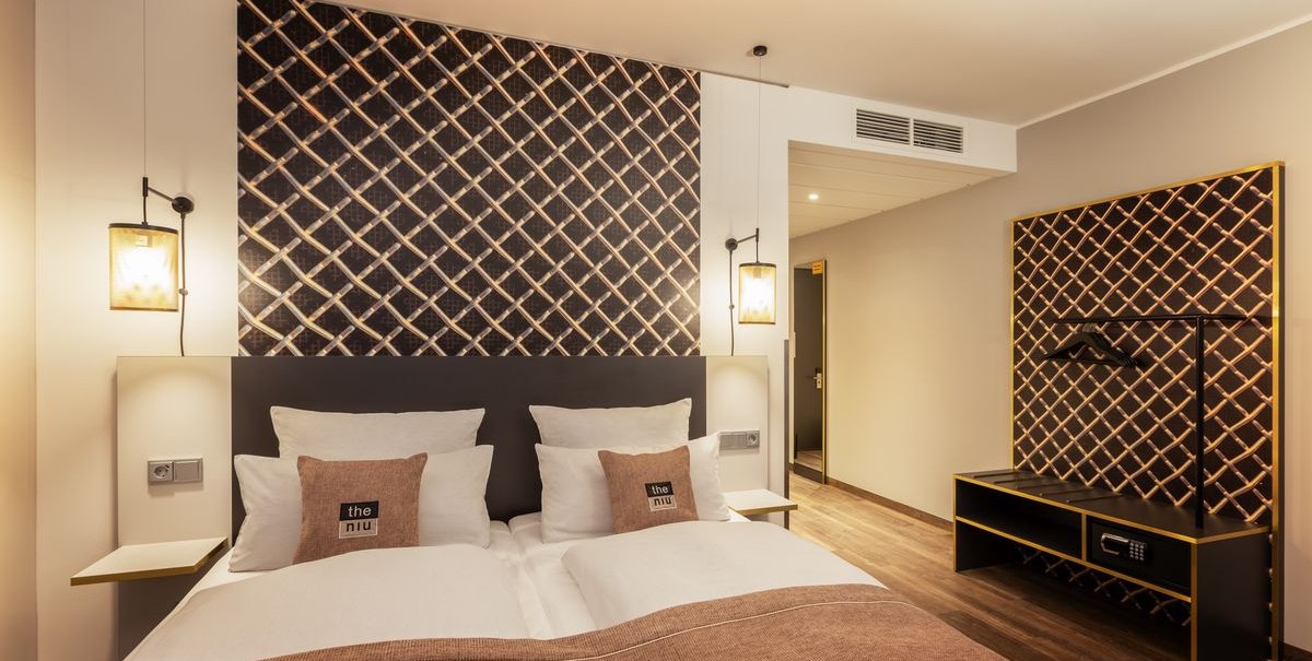 Modernes Hotelzimmer mit Doppelbett, stilvoller Wanddekoration und Holzfußboden. Dezente Beleuchtung und minimalistische Einrichtung., © Novum Hospitality