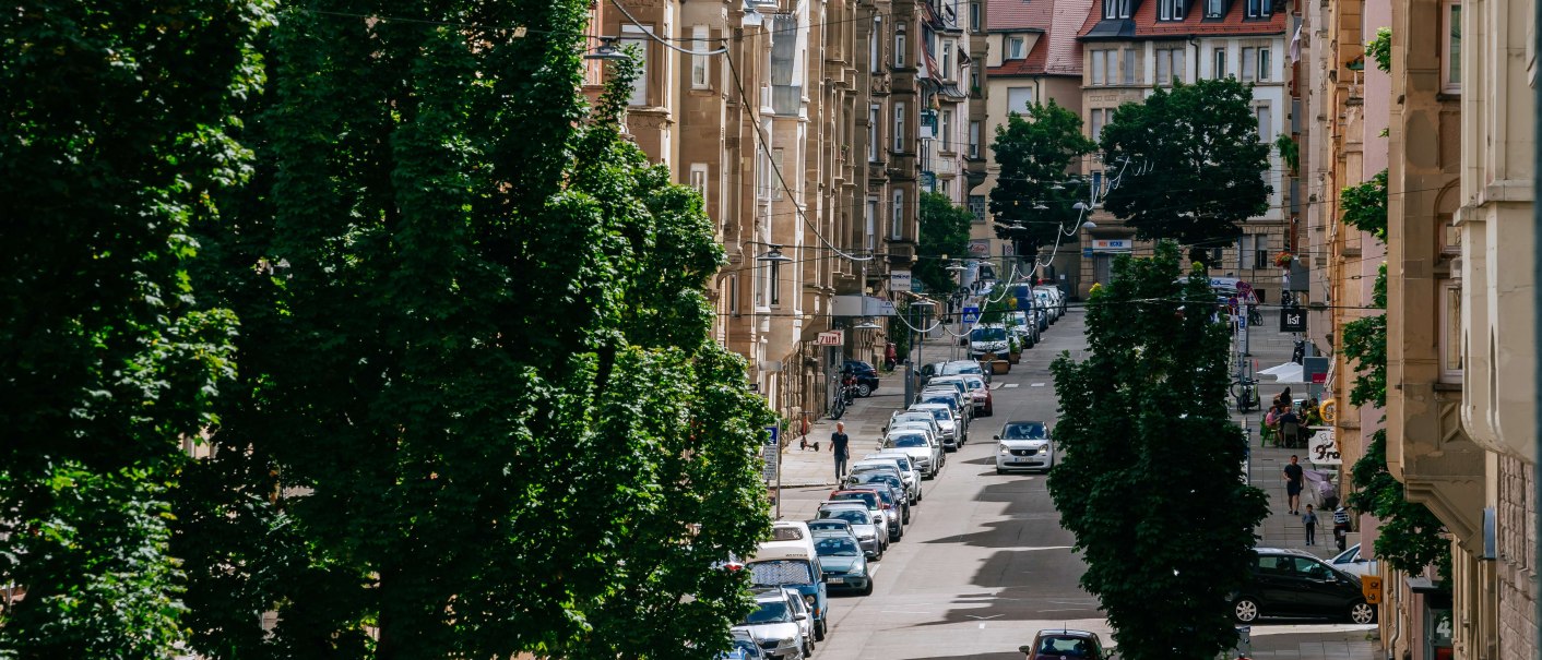 Eine belebte Stadtstraße mit geparkten Autos, alten Gebäuden und Bäumen. Im Hintergrund sind Hügel und weitere Häuser zu sehen., © Thomas Niedermüller Eine belebte Stadtstraße mit geparkten Autos, alten Gebäuden und Bäumen. Im Hintergrund sind Hügel und weitere Häuser zu sehen., © Thomas Niedermüller