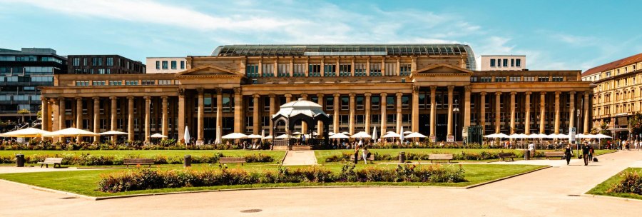 The K&ouml;nigsbau in Stuttgart with its classicist fa&ccedil;ade and glass roof, surrounded by green spaces and walkers in sunny weather., &copy; Stuttgart-Marketing GmbH, Sarah Schmid