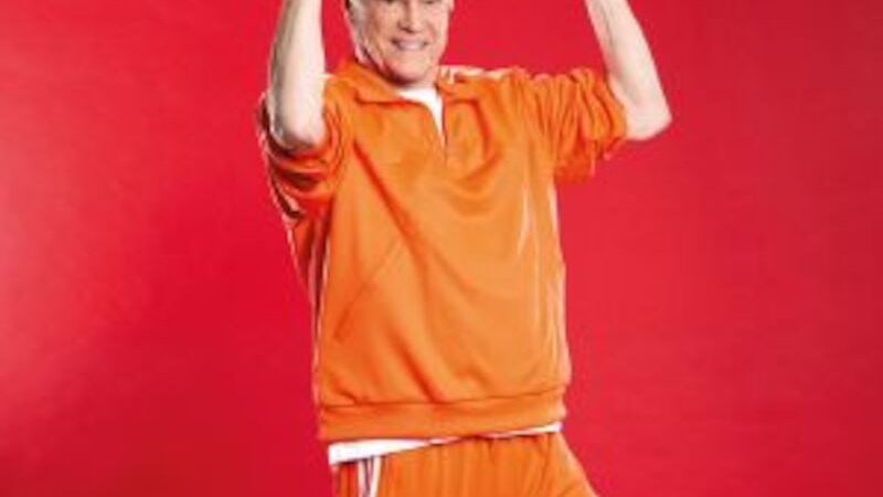 Person in orangem Trainingsanzug hebt Hanteln vor rotem Hintergrund. Sie lächelt und wirkt aktiv und sportlich., © Altes Schauspielhaus und Komödie im Marquardt e.V. Person in orangem Trainingsanzug hebt Hanteln vor rotem Hintergrund. Sie lächelt und wirkt aktiv und sportlich., © Altes Schauspielhaus und Komödie im Marquardt e.V.