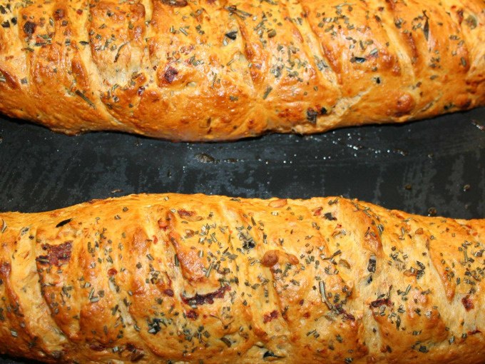 Two golden-brown baguettes with herbs and spices, freshly baked on a black baking tray., &copy; Kultweine-Kochwelten-Kunst&uuml;cke - Kochschule Sonja Lenz