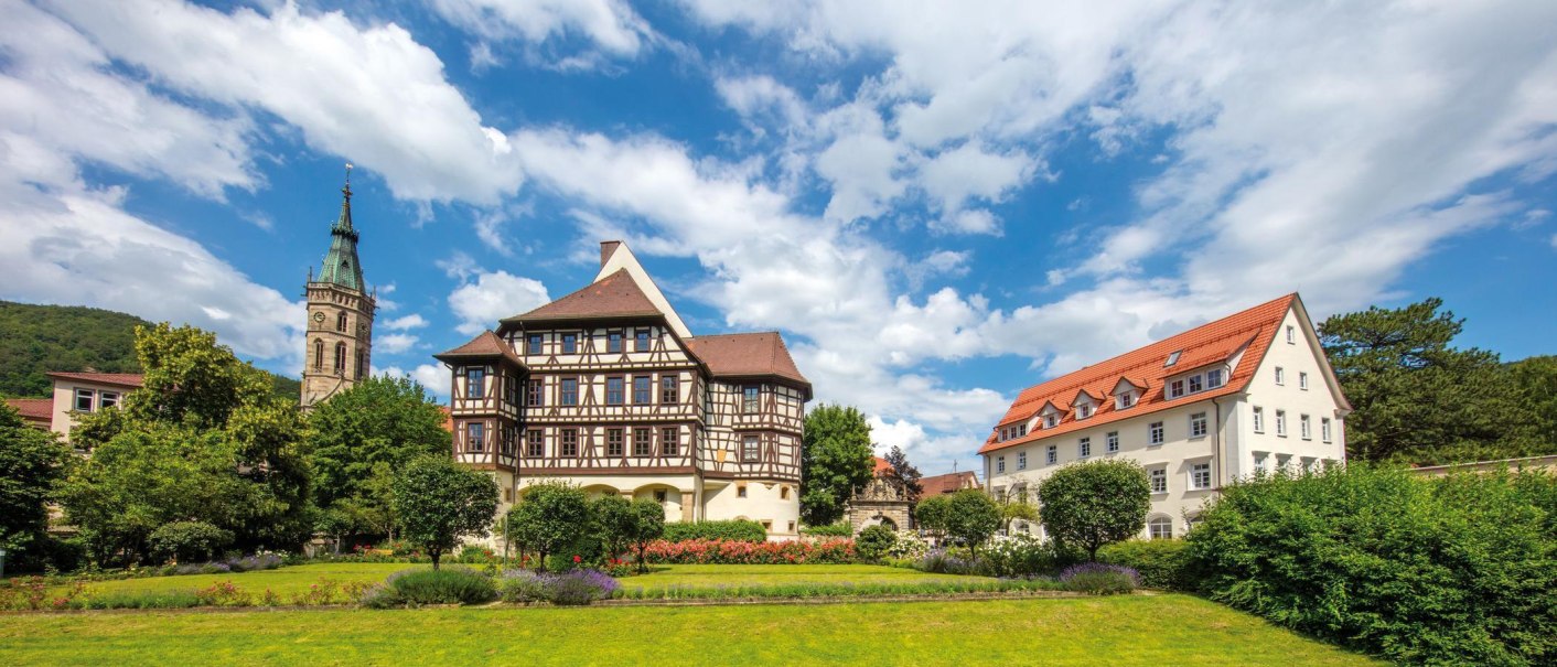 The Bad Urach Residential Palace, with its distinctive half-timbered facade and a tower, surrounded by blooming gardens and trees, under a clear blue sky., © © Stuttgart-Marketing GmbH The Bad Urach Residential Palace, with its distinctive half-timbered facade and a tower, surrounded by blooming gardens and trees, under a clear blue sky., © © Stuttgart-Marketing GmbH
