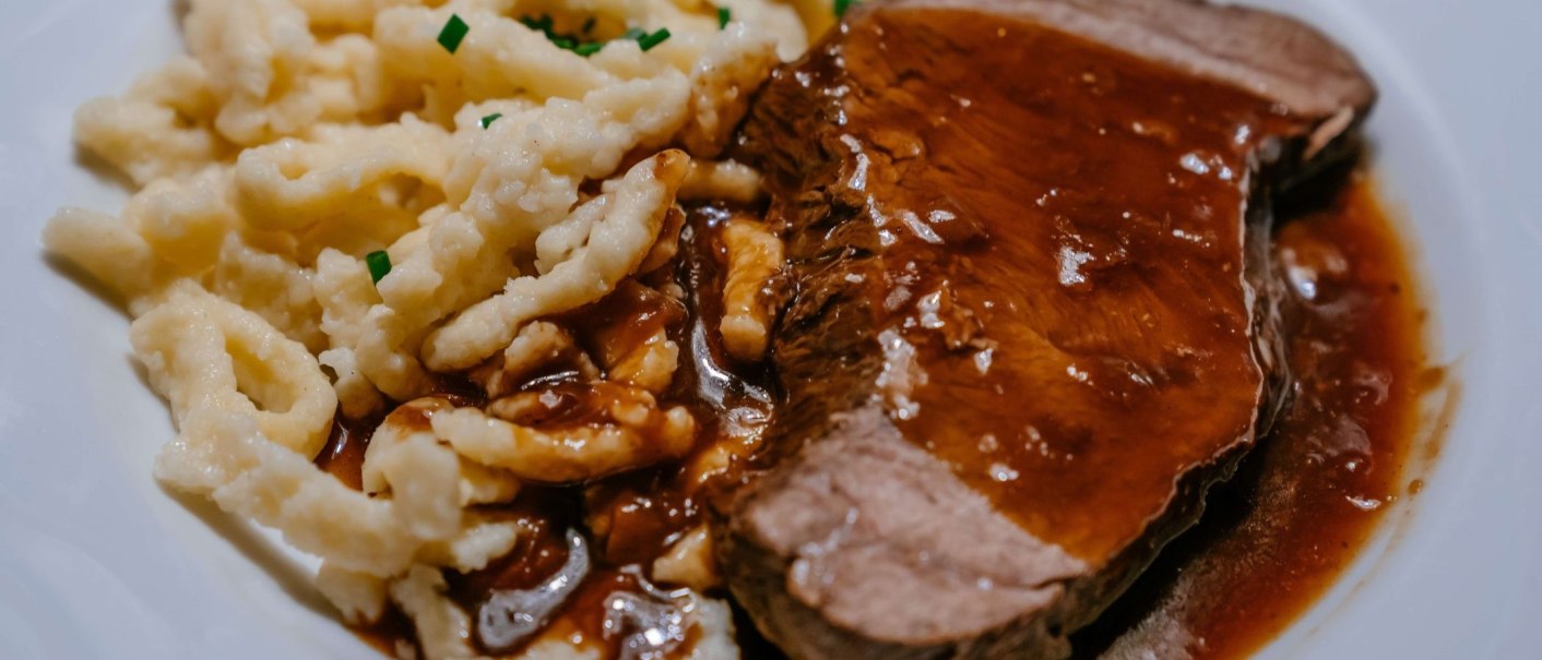 Ein Teller mit Spätzle und einem Stück Braten, übergossen mit dunkler Soße. Die Spätzle sind mit Schnittlauch garniert., © Thomas Niedermüller Ein Teller mit Spätzle und einem Stück Braten, übergossen mit dunkler Soße. Die Spätzle sind mit Schnittlauch garniert., © Thomas Niedermüller