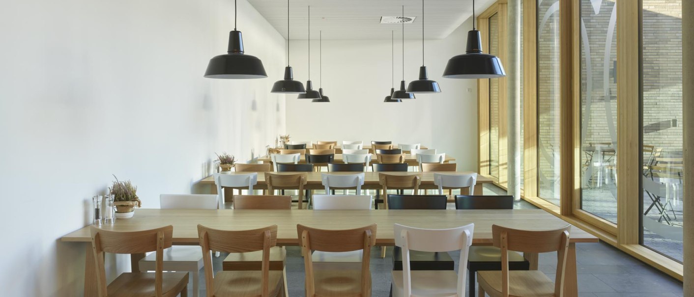 A modern restaurant with wooden tables and chairs, large windows, and hanging black lamps., &copy; TOMAS