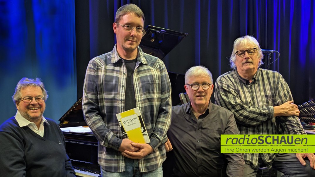 Vier M&auml;nner vor einem Klavier auf einer B&uuml;hne. Einer h&auml;lt ein Buch mit dem Titel 'Wildnis'. Im Hintergrund ein blauer Vorhang., &copy; Freies Radio f&uuml;r Stuttgart