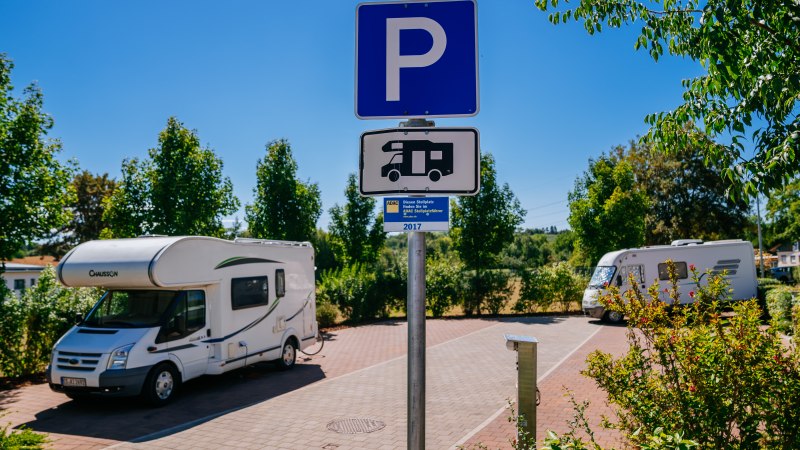 Wohnmobilstellplatz mit zwei geparkten Wohnmobilen und einem Parkplatzschild. Umgeben von Bäumen und sonnigem Wetter., © Stuttgart-Marketing GmbH, Thomas Niedermüller