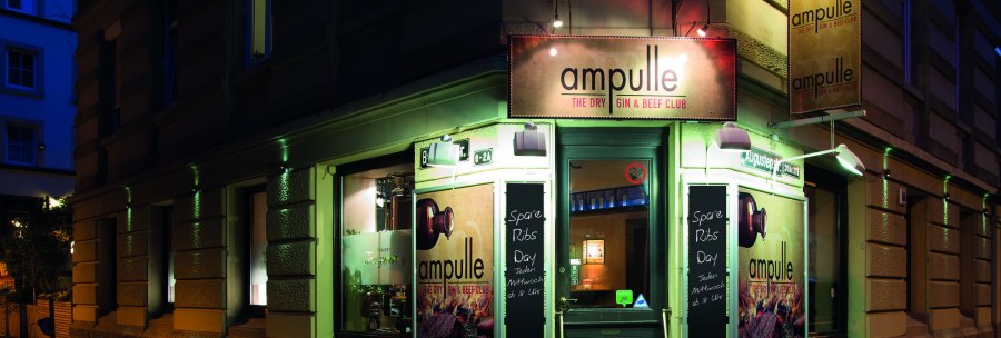 Eingang des Ampulle Gin & Beef Clubs bei Nacht, beleuchtetes Schild und Werbetafeln f&uuml;r Spare Ribs Day. Geb&auml;ude an einer Stra&szlig;enecke., &copy; &copy; Buschwerk Mediendesign-Wilhelmer Gastronomie