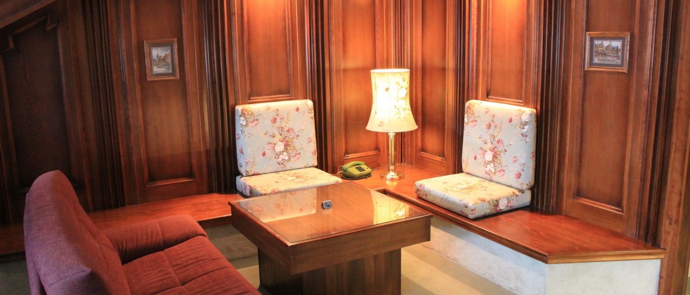 A cozy sitting area with wooden walls, floral-patterned pillows, a table, and a lamp. There is a telephone on the table., &copy; Hotel Spahr