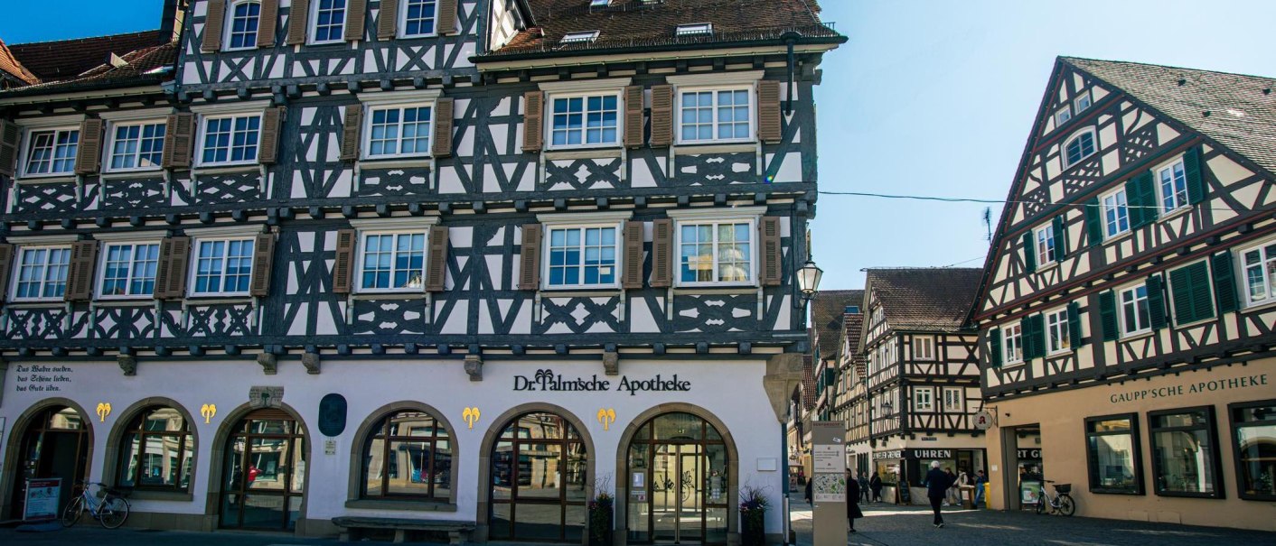 Half-timbered houses on the market square in Schorndorf. Two pharmacies on the first floor, passers-by and bicycles. Sunny day with a clear sky., © Stuttgart-Marketing GmbH, Sarah Schmid Half-timbered houses on the market square in Schorndorf. Two pharmacies on the first floor, passers-by and bicycles. Sunny day with a clear sky., © Stuttgart-Marketing GmbH, Sarah Schmid