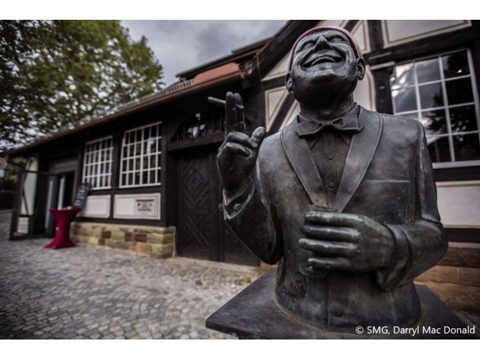 Bronzestatue eines lachenden Mannes mit Fliege vor einem historischen Fachwerkgebäude. Kopfsteinpflaster im Vordergrund, Bäume im Hintergrund., © Stuttgart Marketing GmbH Bronzestatue eines lachenden Mannes mit Fliege vor einem historischen Fachwerkgebäude. Kopfsteinpflaster im Vordergrund, Bäume im Hintergrund., © Stuttgart Marketing GmbH