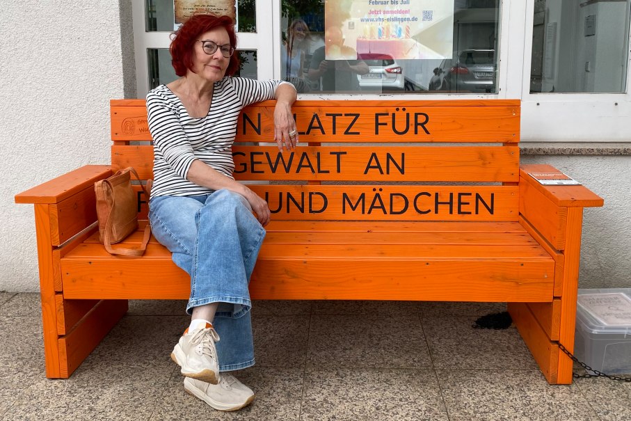 Eine Frau mit rotem Haar und Brille sitzt auf einer orangefarbenen Bank mit der Aufschrift 'Kein Platz f&uuml;r Gewalt an Frauen und M&auml;dchen'., &copy; Foto: T. Faupel