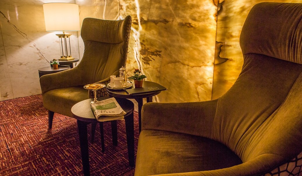 Zwei bequeme Sessel in einer elegant beleuchteten Lobby, mit Tisch, Zeitung und Getränken. Warme, einladende Atmosphäre., © Hotel Royal