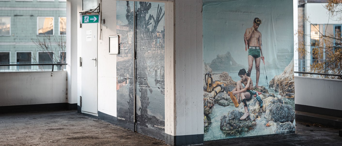 Wandbild in einem Parkhaus zeigt zwei Männer in Badebekleidung mit Tauchausrüstung. Im Hintergrund ein Gebäude mit Fenstern., © SMG Stuttgart Marketing GmbH -Sarah Schmid