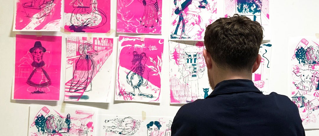 Ein Mann steht vor einer Wand mit pinkfarbenen Kunstwerken, die verschiedene Figuren und Szenen zeigen., © StadtPalais Ein Mann steht vor einer Wand mit pinkfarbenen Kunstwerken, die verschiedene Figuren und Szenen zeigen., © StadtPalais